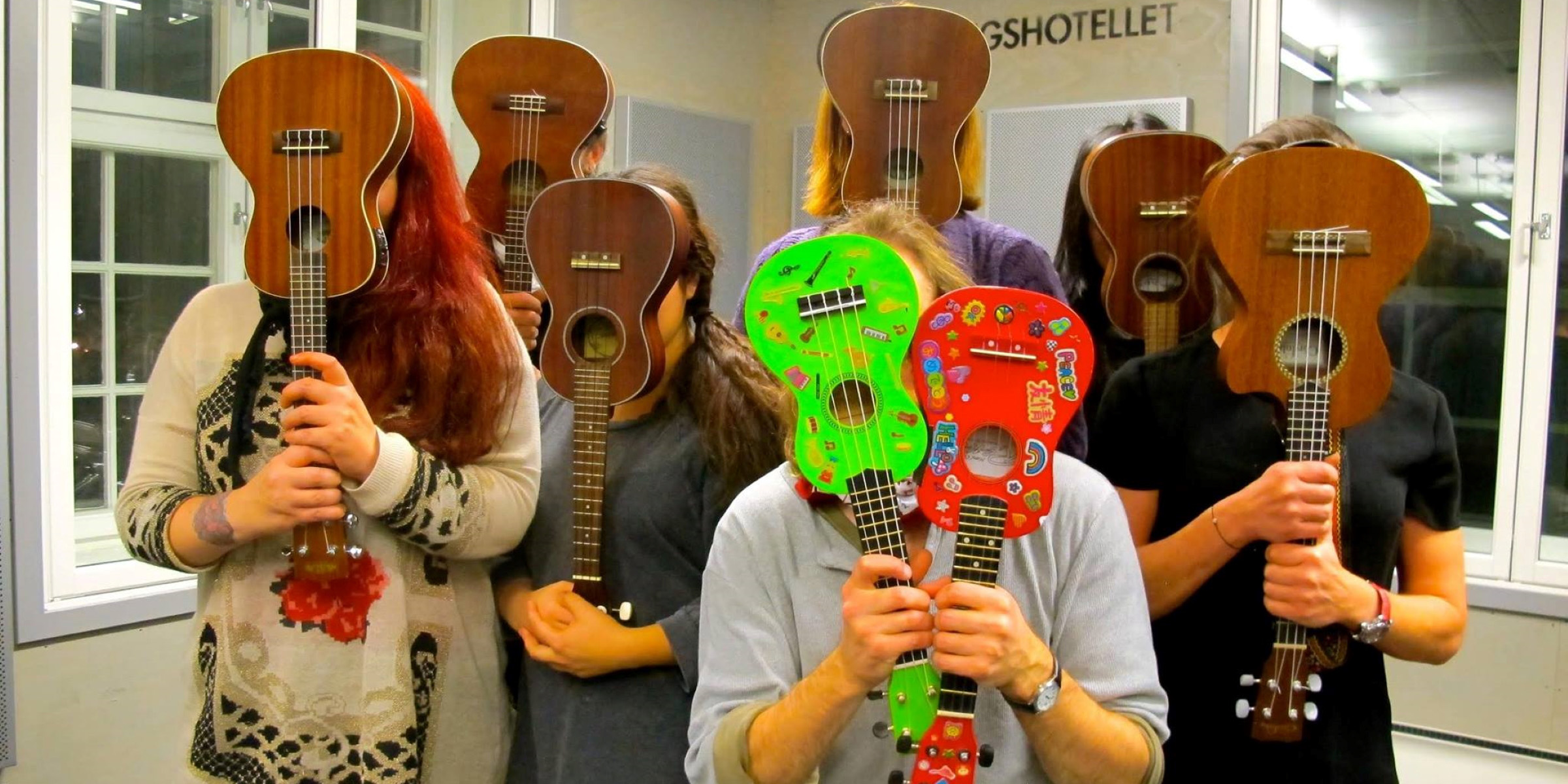 En gruppe mennesker som holder ukuleler opp foran ansiktene sine.
